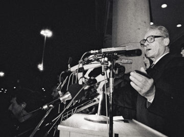 Schwarz-Weiß-Aufnahme von Willy Brandt aus dem Jahre 1989 vor einer Vielzahl von Mikrofonen bei einer Kundgebung vor dem Rathaus Schöneberg zum Fall der Berliner Mauer.